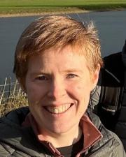 Headshot of Eileen Nutting photographed outdoors with green grassland and a body of water visible in the background